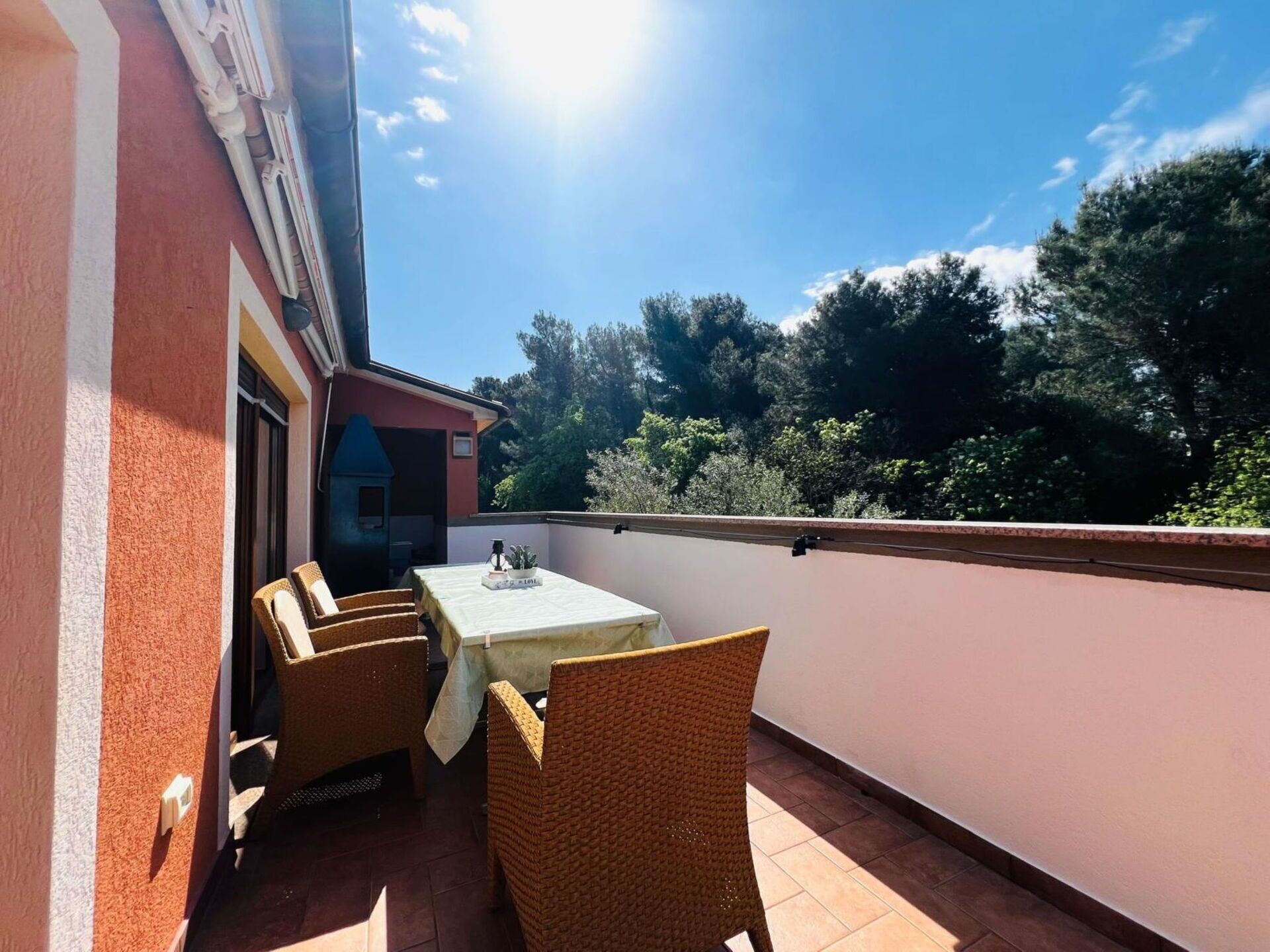 Un balcon avec une table et deux chaises, un immeuble rouge et une vue sur les arbres.