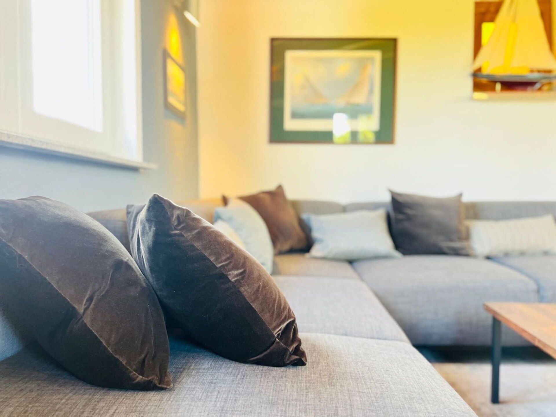 Un salon moderne avec un canapé, des coussins, un tableau et une lampe.