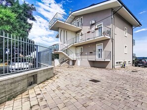 Un edificio residencial de varios pisos con balcones, un camino de entrada con portón y un patio empedrado.