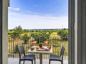 Ein Balkon mit Tisch für zwei Personen, mit Blick auf Weinberge und entfernte Gebäude.