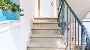 A staircase with a handrail, a door at the top, and a blue planter with plants on the left.