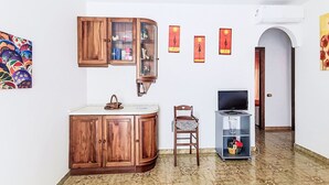Huoneessa on puinen kaappi, tuoli, television alusta ja laatoitettu lattia.