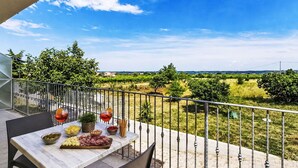 A terrace with a table set for a meal, a railing, and a view of a green landscape.