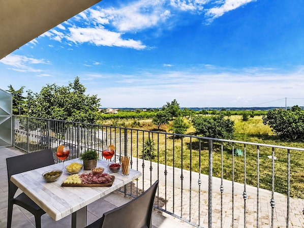 Una terraza con una mesa lista para comer, una barandilla y vistas a un paisaje verde.