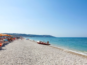 Una playa de guijarros con sombrillas y barcos.