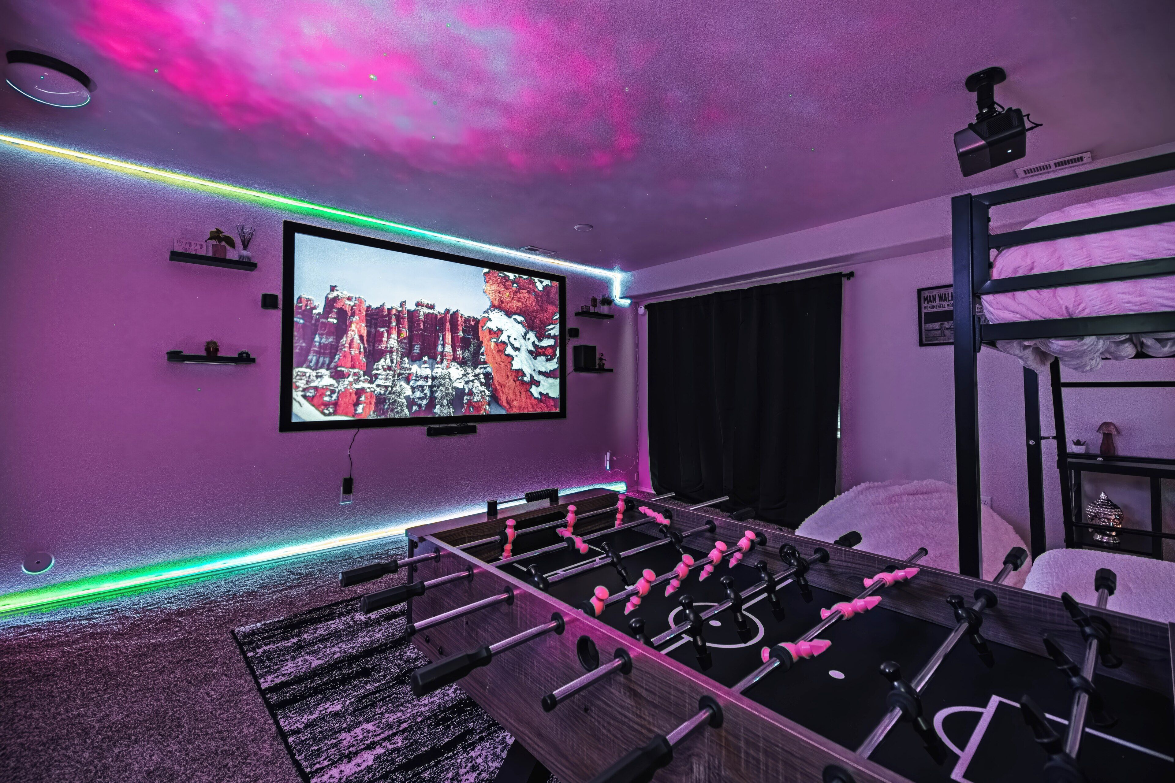 Een kamer met een tafelvoetbaltafel, een grote televisie aan de muur en een stapelbed.