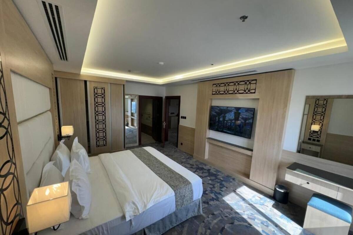 A hotel room with a bed, bedside table, lamp, TV, and a large window.