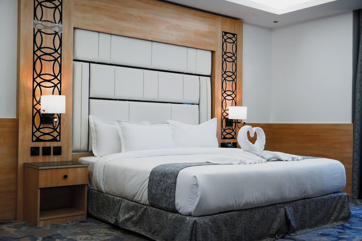 A hotel room with a large bed, bedside lamps, a wooden headboard, and a nightstand.