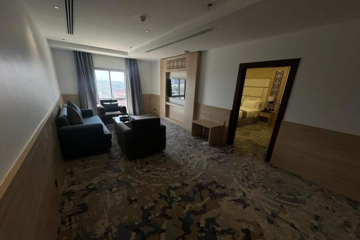 A hotel room with a large bed, a seating area with sofas, a small table, and a view of the city.