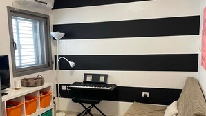 Et værelse med en stribet væg i sort og hvid, et vindue med persienner, et skrivebord med et tastatur, en sofa og opbevaringskasser.