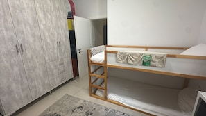 Een stapelbed met houten frame, een kledingkast met meerdere lades en een betegelde vloer.