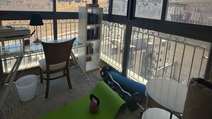 En balkon med udsigt over et bakket landskab, et bord, en stol, en reol og en kettlebell på en måtte.