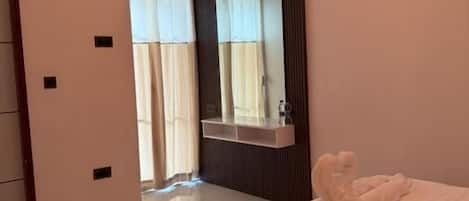 Quarto de hotel com uma cama grande, um espelho, um guarda-roupa e um banheiro visível através de uma porta aberta.