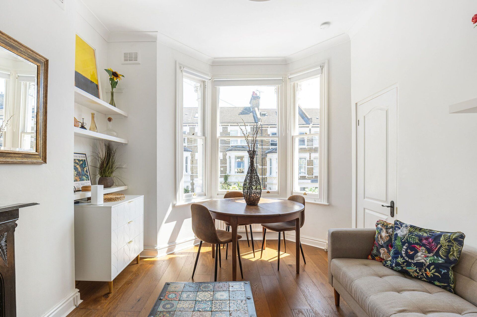 A room with a dining table, chairs, a sofa, a fireplace, and a view of buildings through large windows.