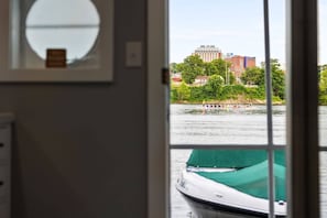 Vista a través de una ventana de un barco sobre el agua, con un edificio y árboles al fondo.
