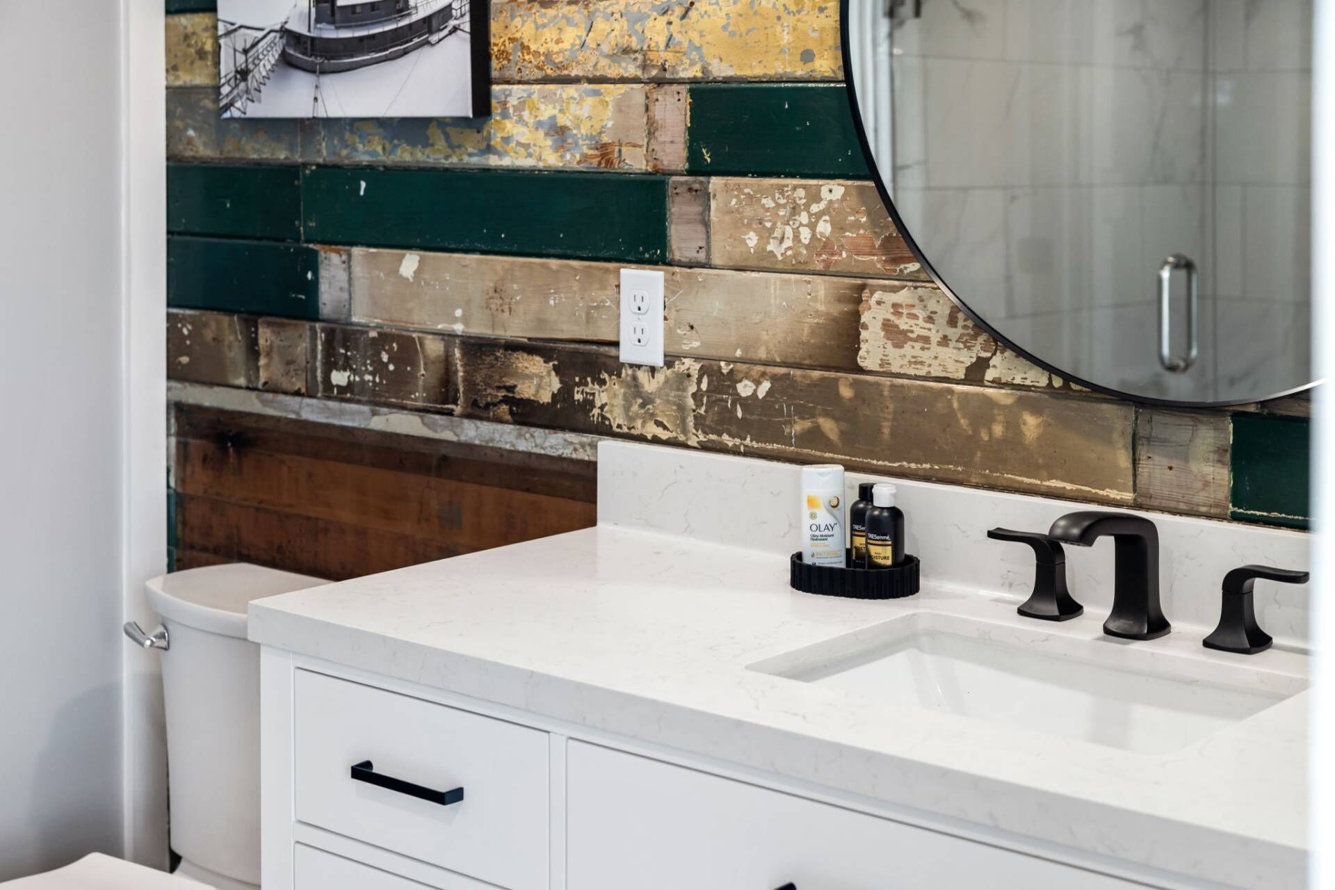 A bathroom with a white sink, two black faucets, a white toilet, and a mirror.