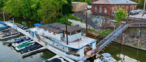 Ein an einem Steg festgemachtes Hausboot mit einer überdachten Terrasse und einer Treppe, die zum Oberdeck führt, sowie ein Steg mit mehreren kleineren Booten.