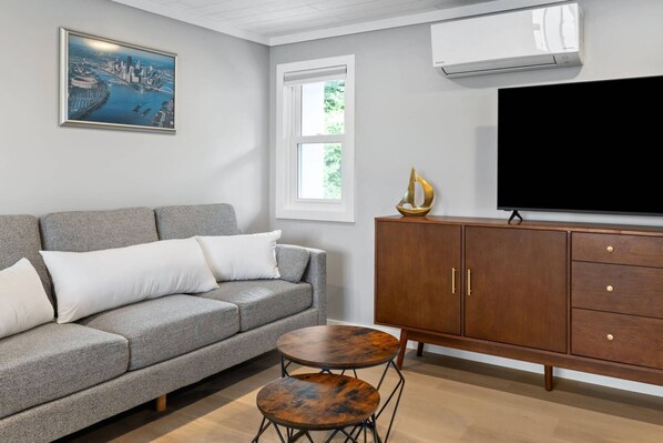 A living room with a grey sofa, two white pillows, a wooden cabinet, a TV, and a painting of a cityscape.