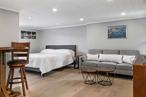 A room with a bed, a gray sofa, a wooden chair, a small round table, and a painting on the wall.