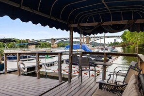 A covered deck with a view of a river, boats, and a bridge.