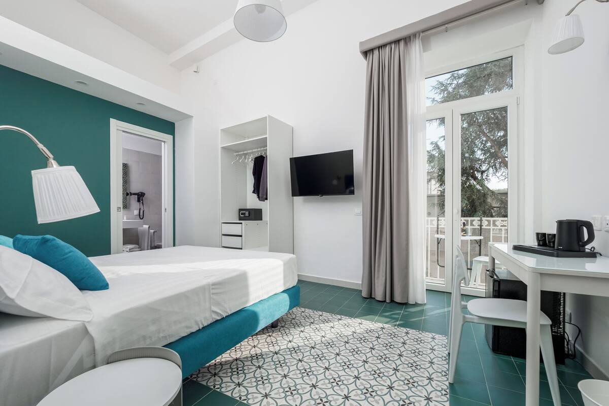 Ein modernes Hotelzimmer mit Bett, Schreibtisch, Fernseher und einem Balkon mit Blick.