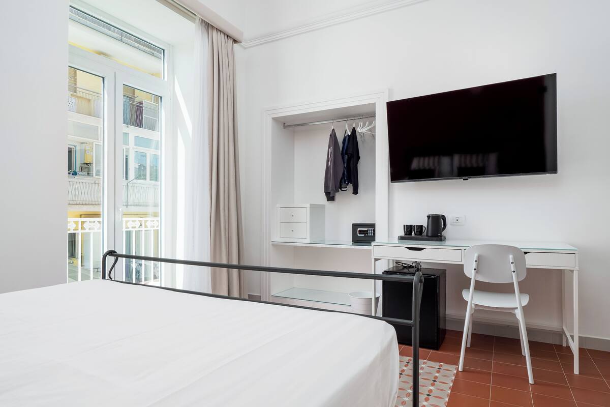 Ein Hotelzimmer mit einem Bett, einem Schreibtisch mit Stuhl, einem Fernseher und einem Fenster mit Vorhängen.