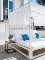 A white outdoor bed with blue pillows, a small table with a vase of flowers, and a white canopy.