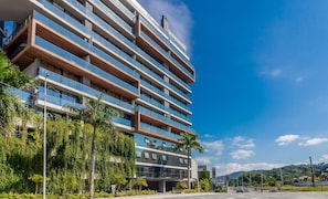 Ein mehrstöckiges Hotel mit Balkonen, umgeben von Grün und wolkenlosem Himmel.