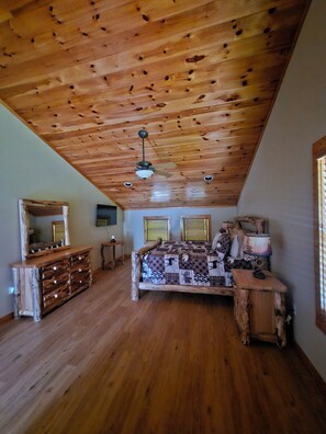 A bedroom with a wooden ceiling, a bed with a patterned blanket, a dresser, and a mirror. - Casa Lago Retreat (Topton)