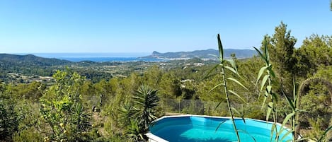 A swimming pool surrounded by lush greenery and a view of a coastal landscape.