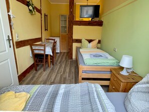 A compact room with a bed, a small table with chairs, a television, and a lamp.