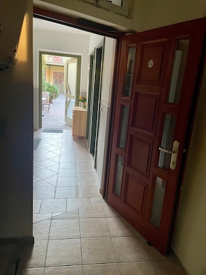 A hallway with a tiled floor, a wooden door, and a view into an outdoor area with a table and chairs.