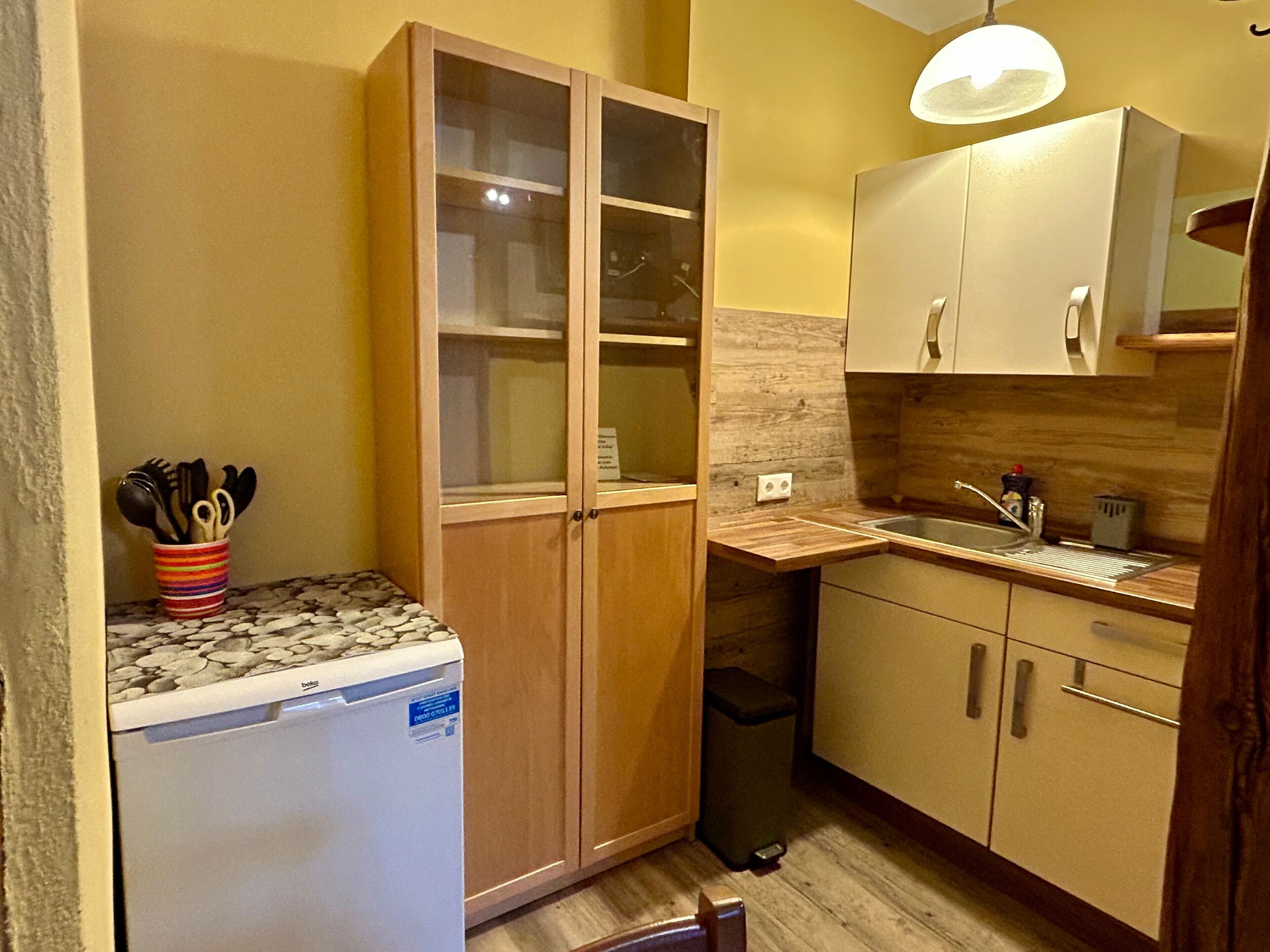 Una cocina compacta con lavavajillas, armarios de madera, una encimera y un lavabo.