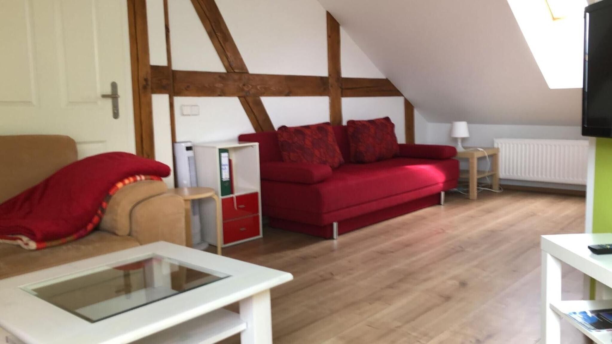Een loft-achtige kamer met een rode bank, een glazen salontafel en een witte kast.