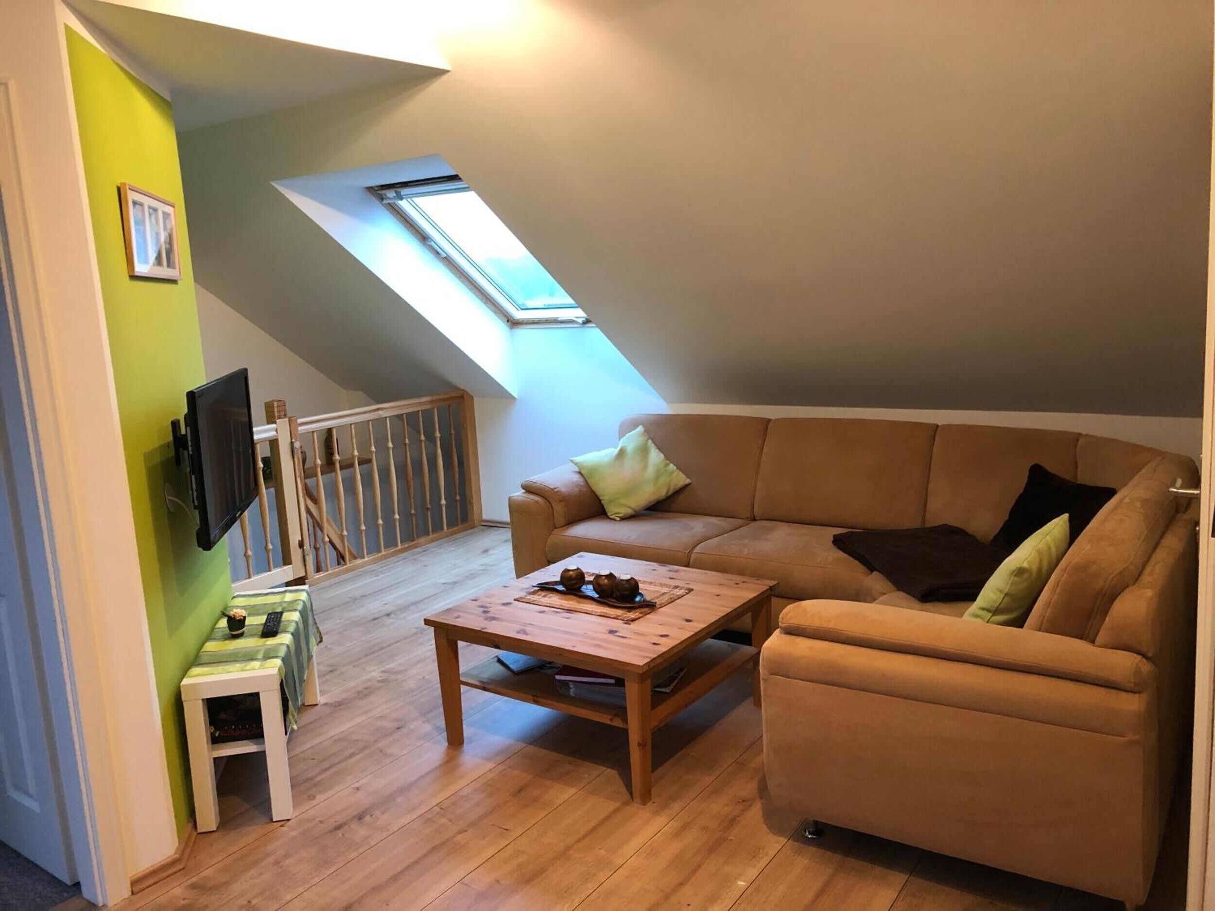 En mysig lägenhet med öppet loft, ett sluttande tak, ett träbord, en brun lädersoffa och en liten träpall.