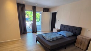 A modern bedroom with a large bed, wooden flooring, and a view of the outdoors. - Cozy and bright apartment in Lahde—in a quiet location, with a fully equipped kitchen (Petershagen)