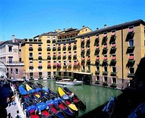 Ein Hotel mit mehreren Balkonen, einem Kanal und vor der Tür vor Anker liegenden Booten.