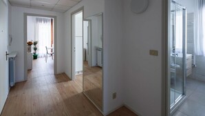 A modern interior with a wooden floor, a dining area with a table and chairs, and a bathroom with a glass shower. - Stylish Lido Beach Apartment with Terrace, Shared Garden & Steps to the Sea (Lido)
