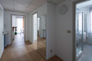Ein modernes Interieur mit Holzboden, einer Essecke mit Tisch und Stühlen sowie einem Badezimmer mit Duschkabine.