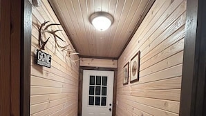 Un corridoio stretto con pareti in legno, una panca, una porta in fondo e un cartello sulla parete sinistra.