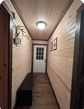 A narrow hallway with wooden walls, a bench, a door at the end, and a sign on the left wall.