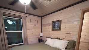 Una camera da letto con un letto, un ventilatore a soffitto, un comodino con una lampada e una finestra.