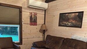 Un soggiorno accogliente con un divano in pelle marrone, un poggiapiedi coordinato, una finestra con persiane, un condizionatore d'aria, una lampada e un quadro appeso al muro.