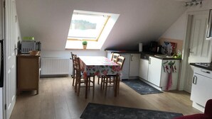 A compact kitchen with a dining table, a radiator, a small window, and a ceiling fan. - Golden Anchor Cozy Holiday Apartment in the Center of Rheinsberg (Rheinsberg)