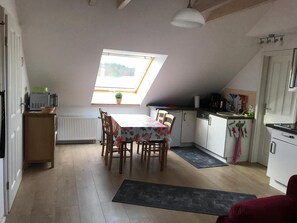 A compact kitchen with a dining table, a radiator, a small window, and a ceiling fan.