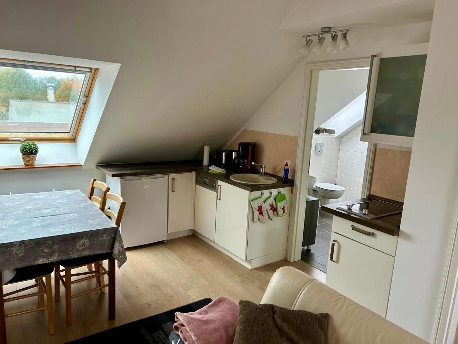 A compact kitchen with a dining table, chairs, a small refrigerator, and a microwave.