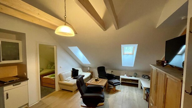 A loft-style room with a high ceiling, exposed beams, a ceiling fan, a television, a sofa, a coffee table, and a small window. - Golden Anchor Cozy Holiday Apartment in the Center of Rheinsberg (Rheinsberg)