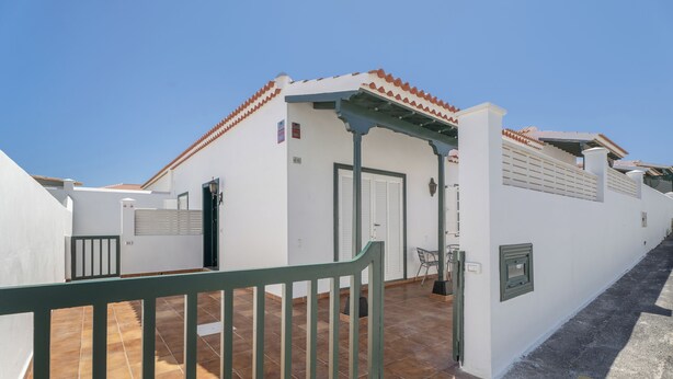 A white building with a tiled roof, a green gate, and a paved courtyard. - Charming Bungalow Rental in Abades, Spain - Perfect Family Retreat (Arico)