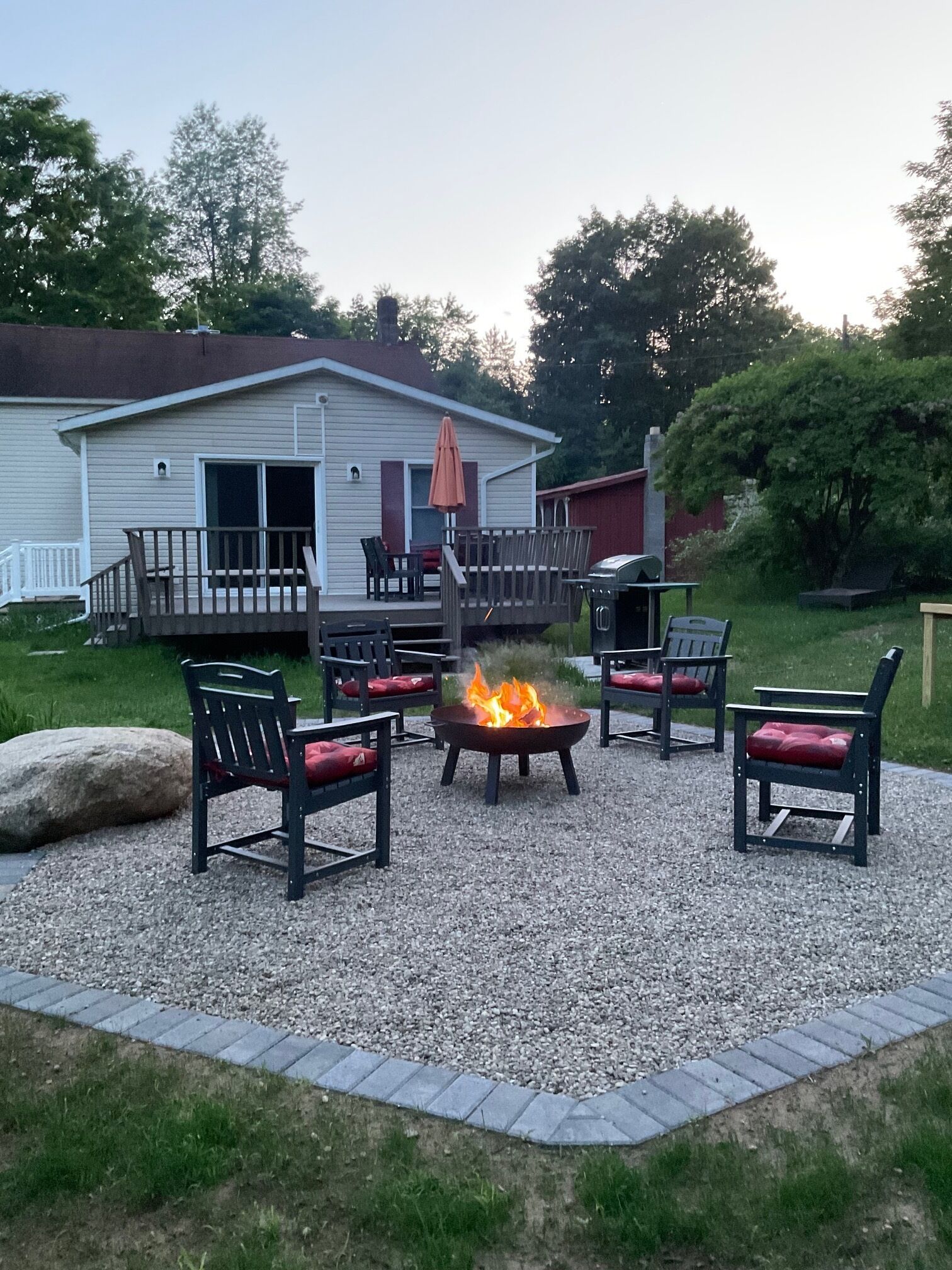 A patio area with a fire pit surrounded by chairs and a grill.