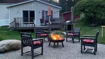 A patio area with a fire pit surrounded by chairs and a grill.